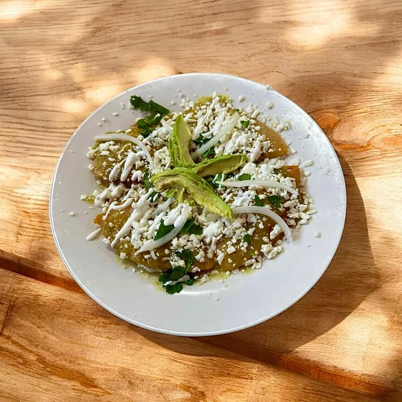 Green enchiladas topped with cream, queso fresco, onion and avocado